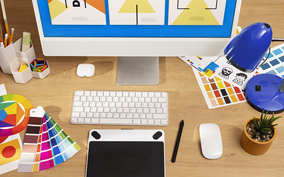 A desk with a monitor, mouse, and keyboard, with color swatches and a drawing tablet for working on graphic designs