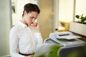 Woman holding paper and looking confused by the printer.