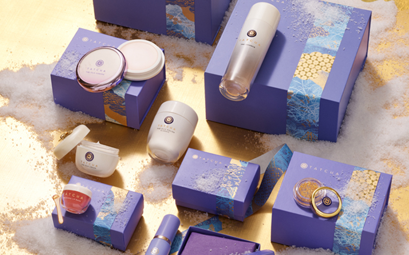Tatcha Packaging flatlay with gold and purple packaging on a gold background. 